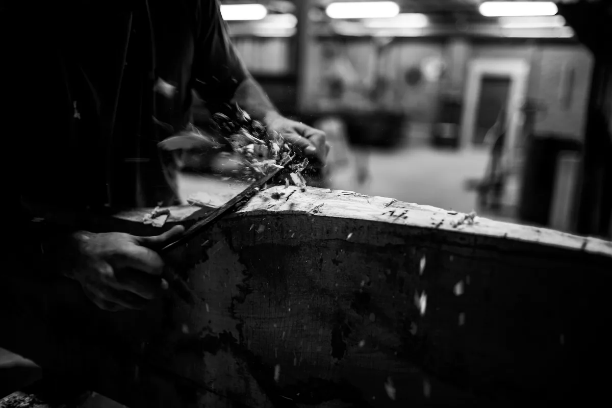Man sieht eine Detailfotografie, wie ein Zimmermann Holz hobelt.
